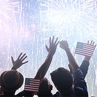 People holding American flags watching fireworks.