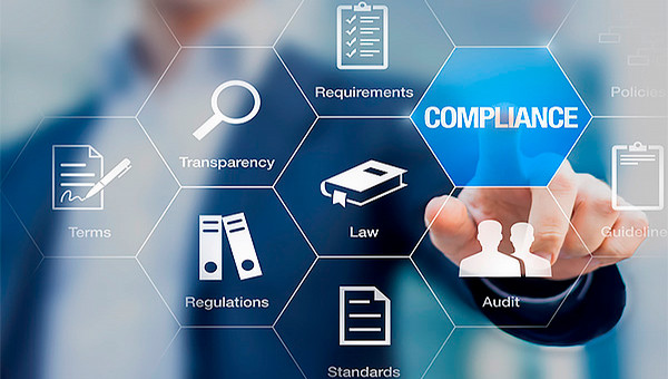 Foreground of white outlined interlocking hexagons, each with an icon related to compliance reporting, such as regulations, terms, transparency, requirements, law, audit, standards, etc. Blurred in the background is a professionally dressed person reaching forward to touch the 'compliance' hexagon, as if hexagons were displayed on a touchscreen.