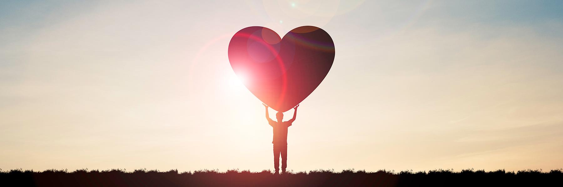 person in a field holding a heart during sunset