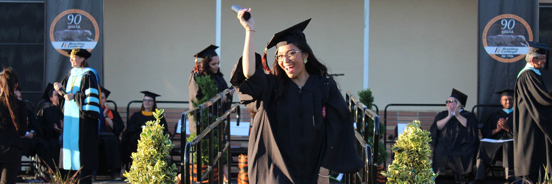 graduation ceremony with student holding up diploma.